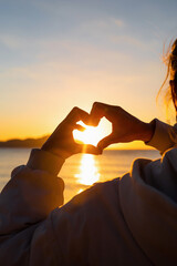 Heart shape with female hands over sunset sky background