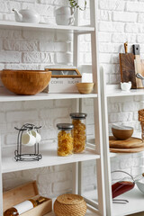 Modern shelf units with kitchenware near white brick wall