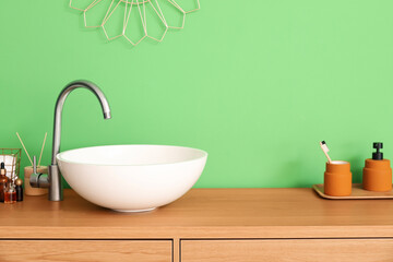 Table with white sink and bath supplies near green wall
