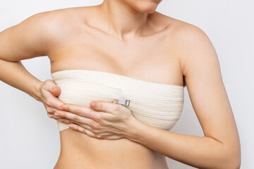 Cropped shot of young woman with elastic bandage after breast augmentation with silicone implants...