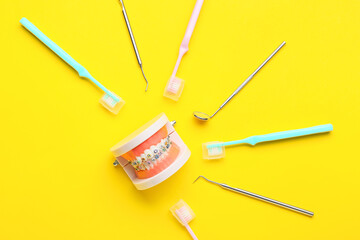 Model of jaw with dental braces, toothbrushes and dentist tools on yellow background