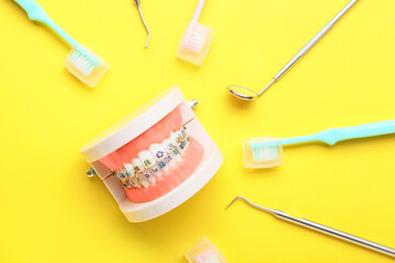 Model of jaw with dental braces, toothbrushes and dentist tools on yellow background