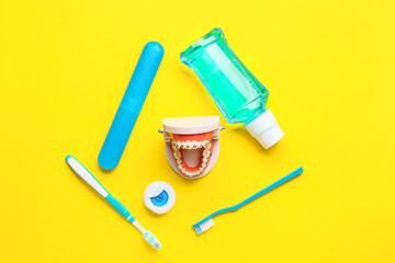 Model of jaw with dental braces, rinse, floss and toothbrushes on yellow background