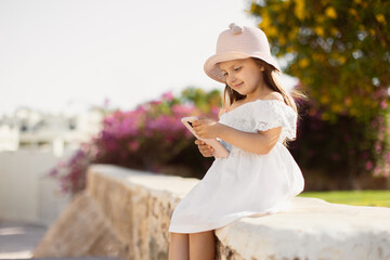 Obraz premium Surprised happy cute blond little girl having video chat with friends and family using smartphone. Four year old caucasian girl is smiling happily as she uses mobile phone to search for information