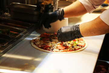 In an Italian restaurant, the pizza master prepares pizza according to customer requests. Special sauce is applied on the pizza dough and pizza ingredients are placed on it. chosen focus