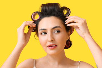 Beautiful young woman in hair rollers on yellow background