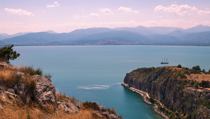 Fototapeta na wymiar Beautiful seascape, rocky hills, small island, lilac sky, and far away is travel boat, Greece