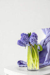 Vase with hyacinth flowers on chair near white wall, closeup