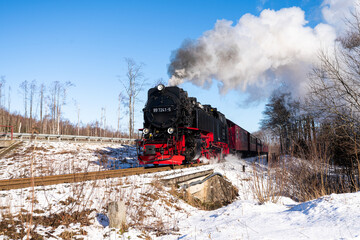Fototapeta na wymiar Historische Dampflokomotive im Schnee mit Dampf auf dem Brocken in Deutschland
