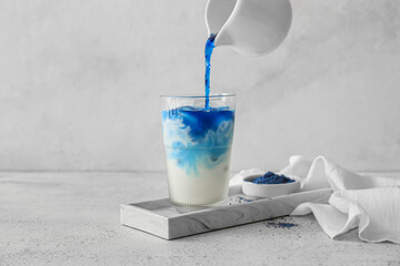 Pouring blue matcha tea in glass with milk on light background