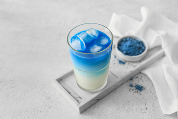 Glass of blue matcha tea and bowl with powder on light background