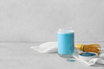 Glass of blue matcha tea, chasen and bowl with powder on light background