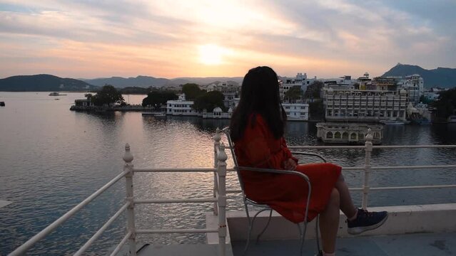 Beautiful Indian female enjoying sunset while sitting near lake Pichola at Udaipur city, Rajasthan, India. Woman relaxing during holidays. Sunset at Udaipur city. People enjoying holidays