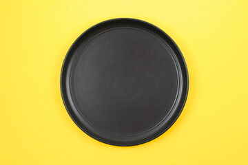Black ceramic plate on a yellow background, top view. Menu concept.