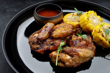 Grilled chicken tobacco, with sauce and corn, on a dark background