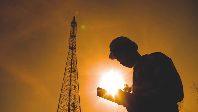silhouette engineer man studying telecommunication tower pillars. concept internet technology tv internet. hard hat worker with digital tablet works lifestyle in the information zone