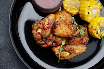 Grilled chicken tobacco, with sauce and corn, on a dark background