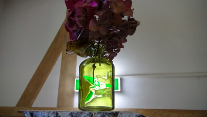 Ein beleuchtetes Fluchtweg Hinweiszeichen leuchtet durch eine grüne transparente Blumenvase....