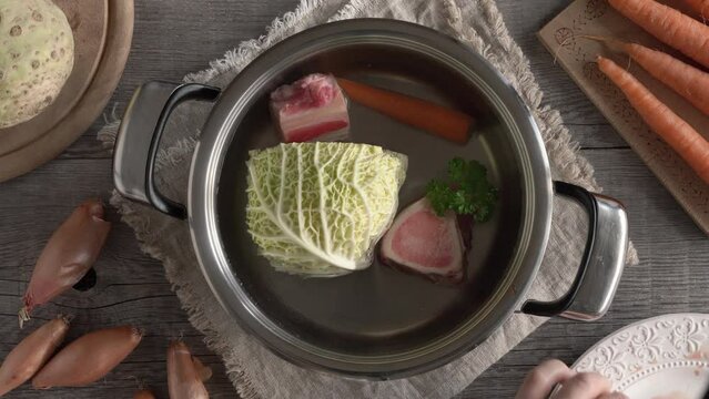 Hands putting beef marrow bones and meat into a pot with water and vegetables - preparation of broth or soup