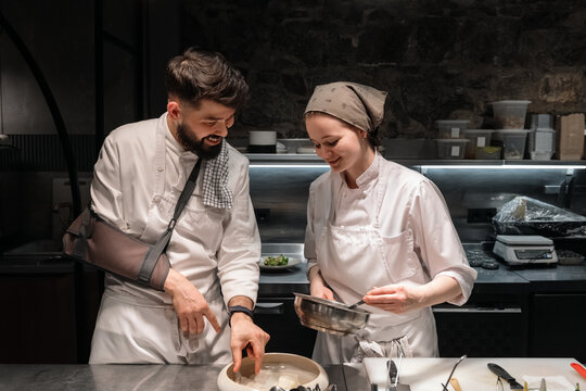 Male chef teaching assistant to cook dish