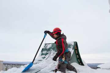 Ice and snow on the roof of the building. Snow removal from the roof. A man removes snow and ice.