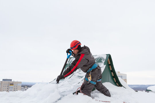 Ice And Snow On The Roof Of The Building. Snow Removal From The Roof. A Man Removes Snow And Ice.