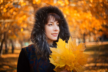A woman with long black hair in the autumn forest holds a bouquet of maple leaves in her hands.