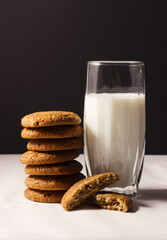 A glass of milk and oatmeal cookies stacked on top of each other. Oatmeal cookies broken in half.