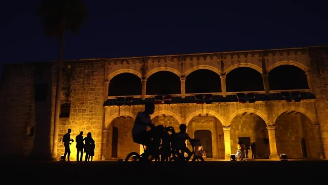 Silhouettes of people on the Plaza de la Hispanidad or Spain with Alc&aacute;zar de Col&oacute;n in the background. Popular tourist attraction in Santo Domingo