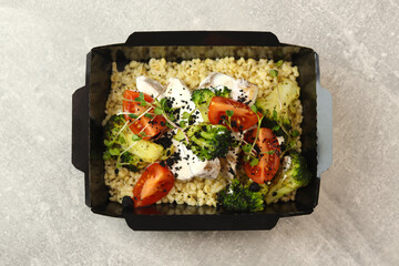 Healthy bowl with bulgur, broccoli, chicken in cream sauce, greens and tomatoes isolated on gray background. Healthy food delivery service and daily ration concept.