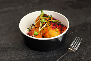 Three meatballs in tomato sauce with wild rice close-up on a black background in eco paper black bowl with fork. Healthy food delivery service and daily ration concept.