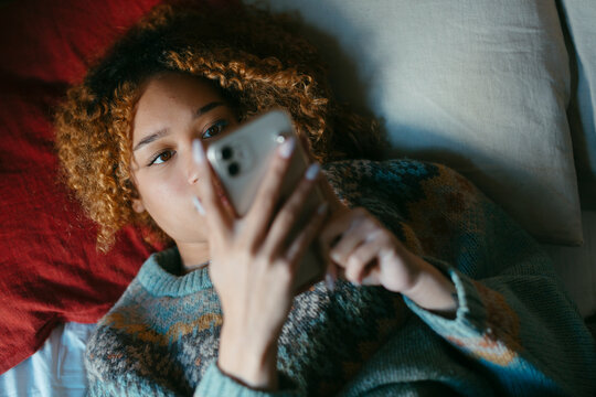 Teenage girl lying on bed checking her smartphone