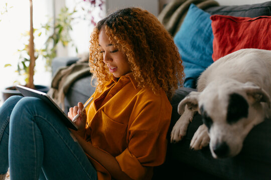 Teenager at home living room using tablet petting dog