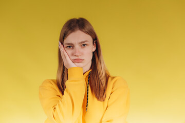 Adorable young teen girl wearing a yellow hoodie. Posing for a photographer on a yellow background. The teenager is worried