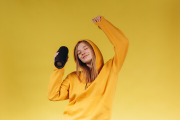 Funny young girl looking, waving hand, holding portable wireless bluetooth music speaker, isolated...