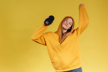 Funny young girl looking, waving hand, holding portable wireless bluetooth music speaker, isolated...