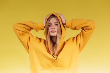 Portrait of sad young teen girl holding hands on head, wearing casual yellow hoodie in tone with background