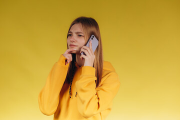 Portrait of a young teen girl holding a phone, a girl talking on the phone, wearing a casual yellow hoodie in one tone with the background