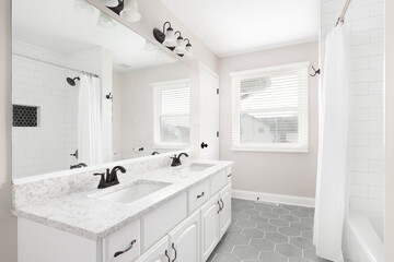 A renovated bathroom with a white vanity, grey hexagon tiled floor, marble countertop, and a shower...