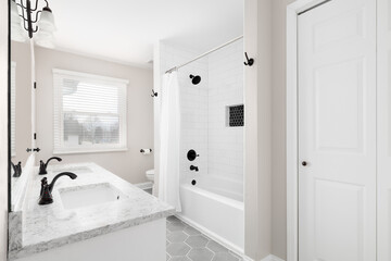 A renovated bathroom with a white vanity, grey hexagon tiled floor, marble countertop, and a shower...