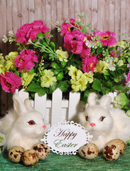  2 decorative  white rabbits ,quail eggs , Happy Easter greeting card on floral background.Easter concept