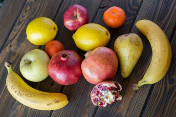 Pomegranates, lemons, bananas, apples, tangerines and pear on a table of wooden planks.