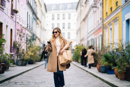 Woman with baguette using smartphone on city street