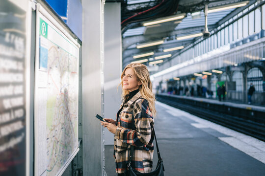 Content female tourist near transit map on platform