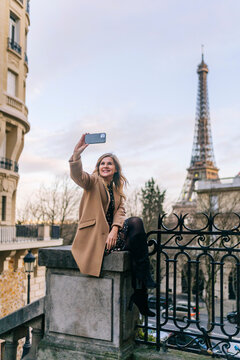 Woman taking selfie on smartphone against Eiffel Tower