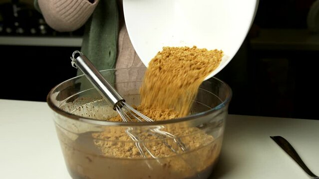 Woman add scrumbled cookies together with melted chocolate in glass bowl for the preparation of typical Piedmontese dessert. Slow motion 4K