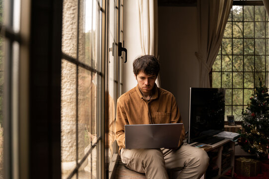 Portrait of man sitting by the window using laptop