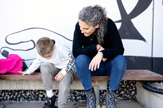 Happy mom sitting near little son wearing inline skates