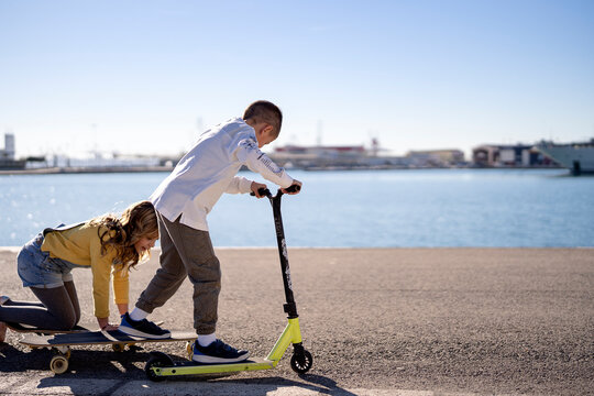 Children riding skateboards with kick scooter near sea