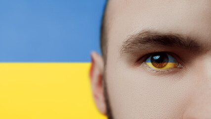 Portrait of a young man with the Ukrainian flag in the eye and in the background. Stop the war in Ukraine. Russia will stop the war.